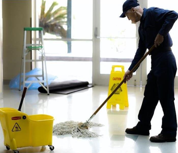 male mopping a white floor with a yellow bucket and sign
